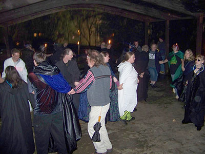 Dancers beneath oaken beams, High Priestess at far right with orb.