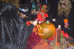 People bending over jack o'lantern and altar, placing objects.