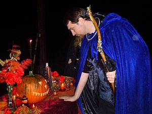 Man in blue cape regards orange jack o'lantern.